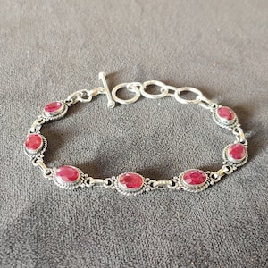 May include: A silver bracelet with a toggle clasp and six oval-shaped red gemstones.