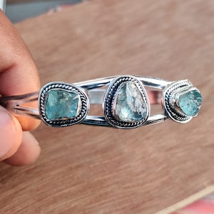 May include: Silver bangle bracelet with three light blue aquamarine gemstones set in silver.