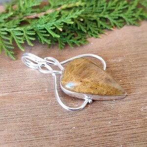 May include: A silver pendant with a teardrop-shaped clear quartz crystal with brown inclusions. The pendant is on a wooden surface.