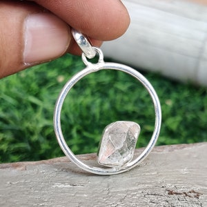 May include: A silver pendant featuring a clear, faceted crystal set within a circular frame.