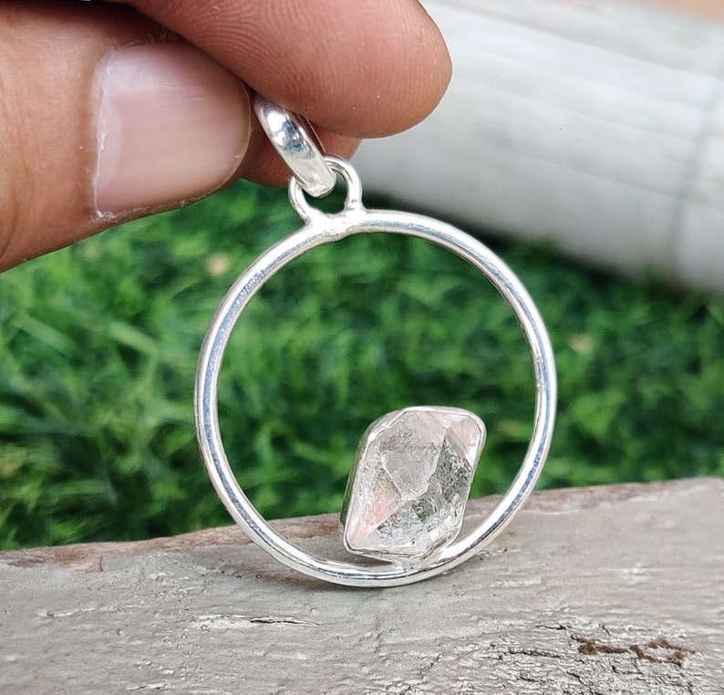 May include: A silver pendant featuring a clear, faceted crystal set within a circular frame.
