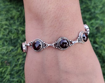 May include: A silver bracelet featuring five round, dark red gemstones. The bracelet has a delicate chain design.