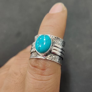 Könnte beinhalten: Ein silberner Ring mit einem Türkis-Stein, der in eine breite Band gefasst ist. Die Band ist mit floralen Designs verziert.