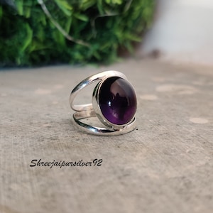 May include: A silver ring featuring a large, round, purple amethyst gemstone. The ring has a simple, modern design with two bands that wrap around the stone.