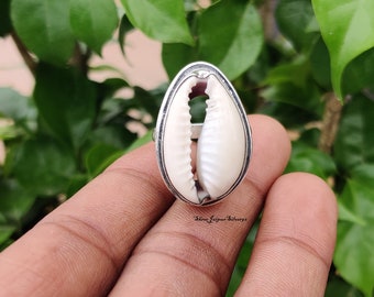 Könnte beinhalten: Ein silberner Ring mit einer weißen Kaurischnecke. Der Ring wird an einem Finger getragen.