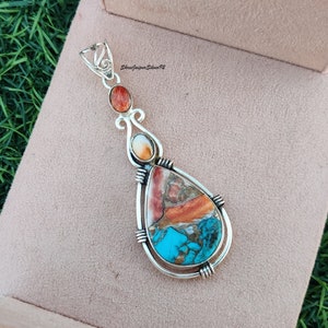 May include: A silver pendant with a teardrop-shaped turquoise and coral stone. The pendant is set in silver and has a bail for attaching a chain.
