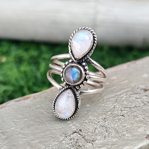 Puede incluir: Un anillo de plata con tres piedras. La piedra central es una labradorita redonda e iridiscente azul. Las dos piedras exteriores son piedras de luna blancas en forma de pera.