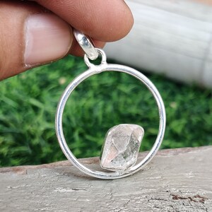 May include: A silver pendant featuring a clear, faceted crystal set within a circular frame.