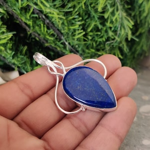 Op de afbeelding: Een zilveren hanger met een traanvormige lapis lazuli-steen in donkerblauwe kleur met gouden vlekken. De hanger is gezet in een zilveren draadframe.