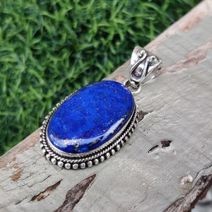 May include: A silver pendant with a large oval lapis lazuli stone. The stone is a deep blue color with gold flecks. The pendant has a detailed silver bail.