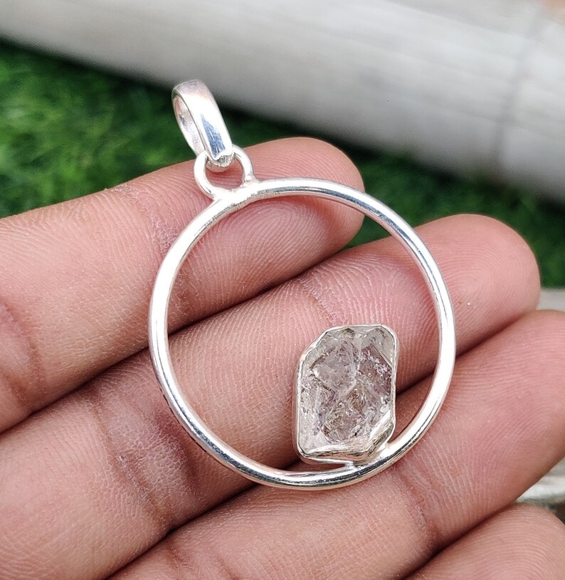 May include: A silver pendant with a clear, faceted crystal set in a circular frame. The pendant is designed to be worn as a necklace.