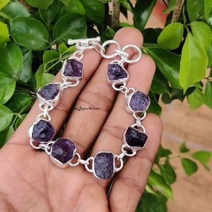 May include: A silver bracelet with a chain link design and seven purple amethyst stones. The stones are rough and have a natural, unpolished look.