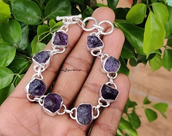 May include: A silver bracelet with a chain link design and seven purple amethyst stones. The stones are rough and have a natural, unpolished look.