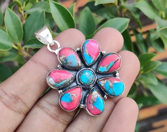 May include: A silver pendant with a flower design. The pendant features a central turquoise stone surrounded by six petals with pink and turquoise stones. The pendant is held by a silver bail.