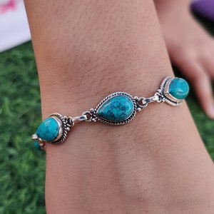May include: A silver bracelet with turquoise stones. The stones are teardrop shaped and have a marbled pattern.
