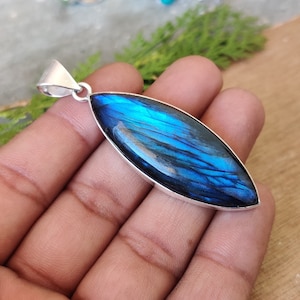 May include: A silver pendant featuring a large, oval-shaped blue labradorite gemstone. The gemstone has a shimmering, iridescent effect.