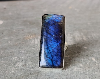 Può includere: Un anello d'argento con una grande pietra rettangolare di labradorite blu. La pietra ha un effetto scintillante e iridescente.