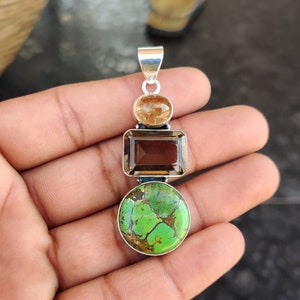 May include: A silver pendant with three gemstones. The top gemstone is a round, light brown stone. The middle gemstone is a rectangular, dark brown stone. The bottom gemstone is a round, green stone.