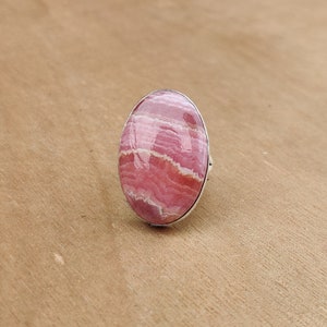 Op de afbeelding: Een zilveren ring met een ovale roze en witte edelsteen. De edelsteen heeft een gestreept patroon.