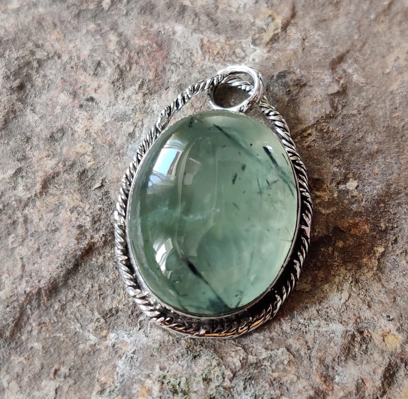 Op de afbeelding: Een zilveren hanger met een groene aventurijn steen gezet in een gedraaid touw ontwerp.