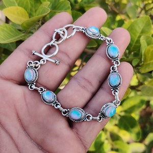 May include: A silver bracelet with a toggle clasp and oval-shaped opal stones. The bracelet is made of sterling silver and features a delicate chain design.