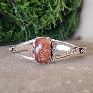 May include: Silver bracelet with a rectangular sunstone gemstone. The bracelet has a delicate, twisted design.
