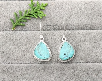 May include: A pair of silver dangle earrings with turquoise stones. The stones are a light blue color and have a slightly irregular shape.