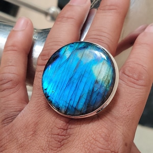 May include: A silver ring with a large, round, blue labradorite gemstone. The gemstone has a iridescent sheen and a unique pattern.