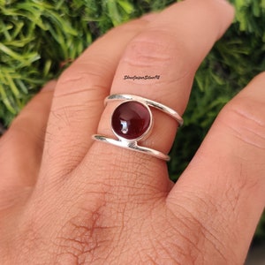 May include: A silver ring with a double band design features a round, dark red gemstone in the center.