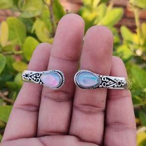 Puede incluir: Un brazalete de plata con dos piedras de ópalo iridiscente en forma de lágrima engastadas en engastes de plata ornamentados.