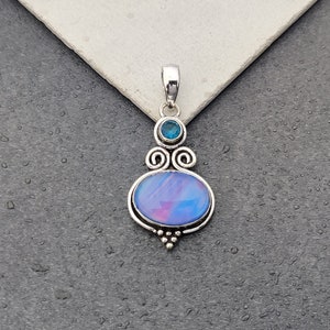 May include: A silver pendant with a blue opal stone and a smaller blue gemstone. The pendant has a swirl design and is set in a silver frame.