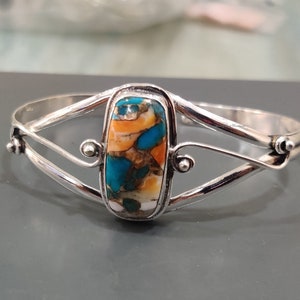 Könnte beinhalten: Silberarmband mit einem bunten Türkis-Stein. Der Stein hat eine Mischung aus blauen, grünen, orangen und weißen Farben.