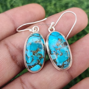 May include: A pair of silver earrings with oval-shaped turquoise stones. The turquoise is a mottled blue and green color with gold flecks.