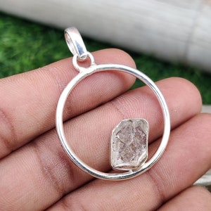 May include: A silver pendant with a clear, faceted crystal set in a circular frame. The pendant is designed to be worn as a necklace.