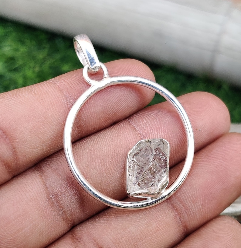 May include: A silver pendant with a clear, faceted crystal set in a circular frame. The pendant is designed to be worn as a necklace.