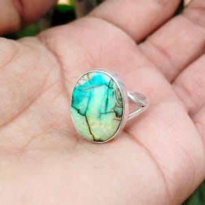 May include: A silver ring with a large oval-shaped green and white opal gemstone.