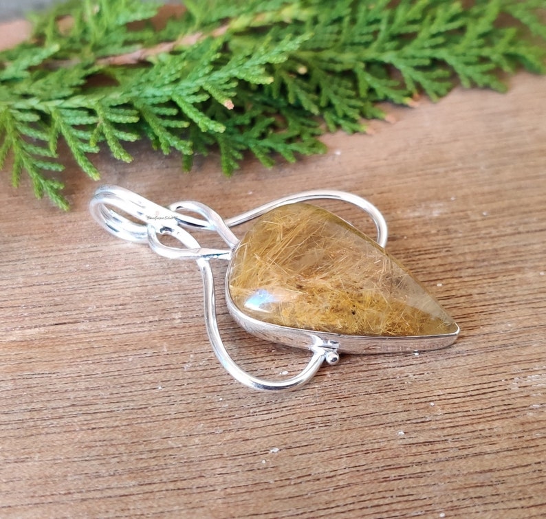 May include: A silver pendant with a teardrop-shaped clear quartz crystal with brown inclusions. The pendant is on a wooden surface.