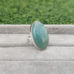 May include: A silver ring with a large oval aquamarine gemstone. The stone is a light blue-green color and has a smooth, polished finish.