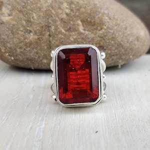 May include: A silver ring with a large, rectangular, red gemstone.