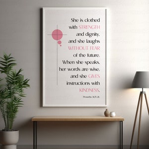Könnte beinhalten: Ein weißer gerahmter Druck mit einem rosafarbenen Kreisdesign und einem Zitat über Stärke, Würde und Freundlichkeit. Das Zitat lautet: "Sie ist bekleidet mit STÄRKE und Würde. und sie lacht OHNE ANGST vor der Zukunft. Wenn sie spricht, sind ihre Worte weise, und sie GIBT Anweisungen mit FREUNDLICHKEIT. Sprichwörter 3:25-26"