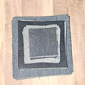 May include: Four squares of denim fabric, stacked on top of each other, with the largest square on the bottom and the smallest square on top. The fabric is a dark blue color and has a slightly textured surface.