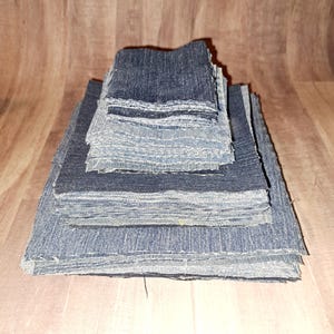 May include: A stack of denim fabric squares in various shades of blue, ranging from dark to light. The squares are stacked in a pyramid shape, with the largest square at the bottom and the smallest square at the top.