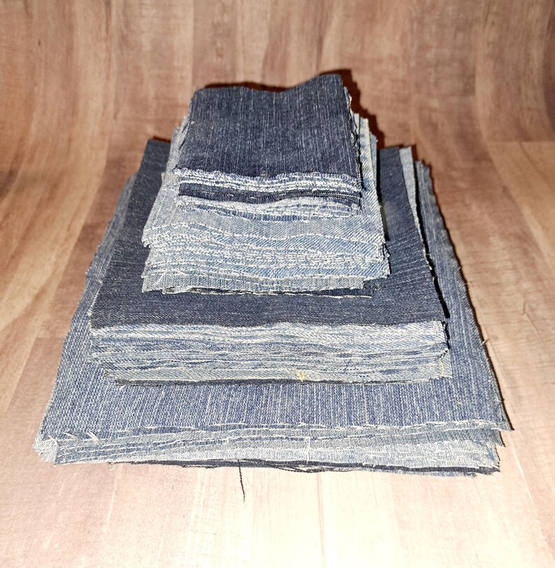 May include: A stack of denim fabric squares in various shades of blue, ranging from dark to light. The squares are stacked in a pyramid shape, with the largest square at the bottom and the smallest square at the top.