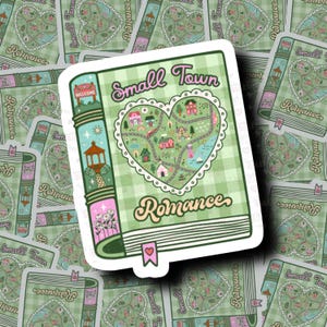 May include: A sticker featuring a book design with the words "Small Town Romance." The book's cover has a heart-shaped map of a town, with houses, roads, and a gazebo. The background is a light green plaid pattern.