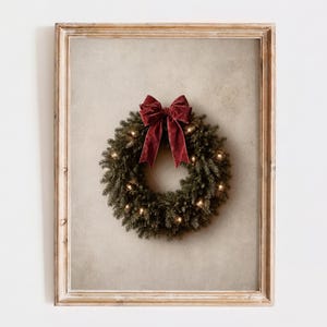 Può includere: Un'opera d'arte da parete incorniciata raffigurante una ghirlanda circolare di sempreverdi decorata con piccole luci bianche calde e un grande fiocco in velluto rosso scuro in alto, su uno sfondo beige chiaro testurizzato.