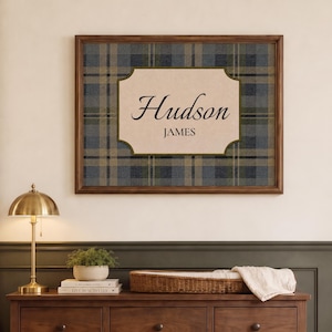 Puede incluir: Un cuadro rectangular con marco que presenta un fondo de cuadros en azul, gris y beige. En el centro, una placa de color crema con un borde verde oscuro muestra el nombre Hudson en letra cursiva y el nombre JAMES en letra con remates.