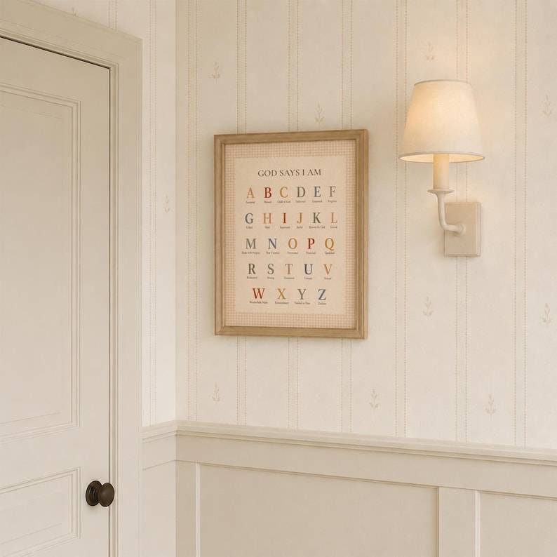 May include: A framed wall art print featuring the alphabet in a grid layout with the text GOD SAYS I AM at the top. Each letter is paired with a descriptive word in a muted color palette, housed in a light wood frame with a textured border.