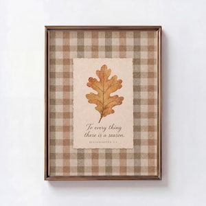 May include: A framed wall art piece featuring a brown and beige gingham background. Centered is a cream-colored paper with a deckled edge, displaying a watercolor oak leaf and the text: To every thing there is a season. ECCLESIASTES 3:1.