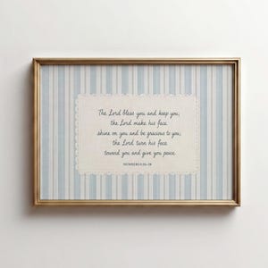Puede incluir: Una pieza de arte mural rectangular en un marco dorado con un fondo de rayas verticales azul claro y blanco. Centrada hay una tarjeta rectangular color crema con un borde de encaje festoneado que contiene el texto Numbers 6:24-26 en letra negra.
