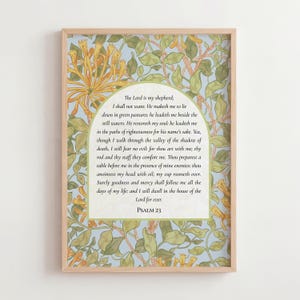 May include: A framed print of Psalm 23, set against a light blue backdrop with a floral pattern in yellow and green. The text is in a traditional font, and the frame is light wood.